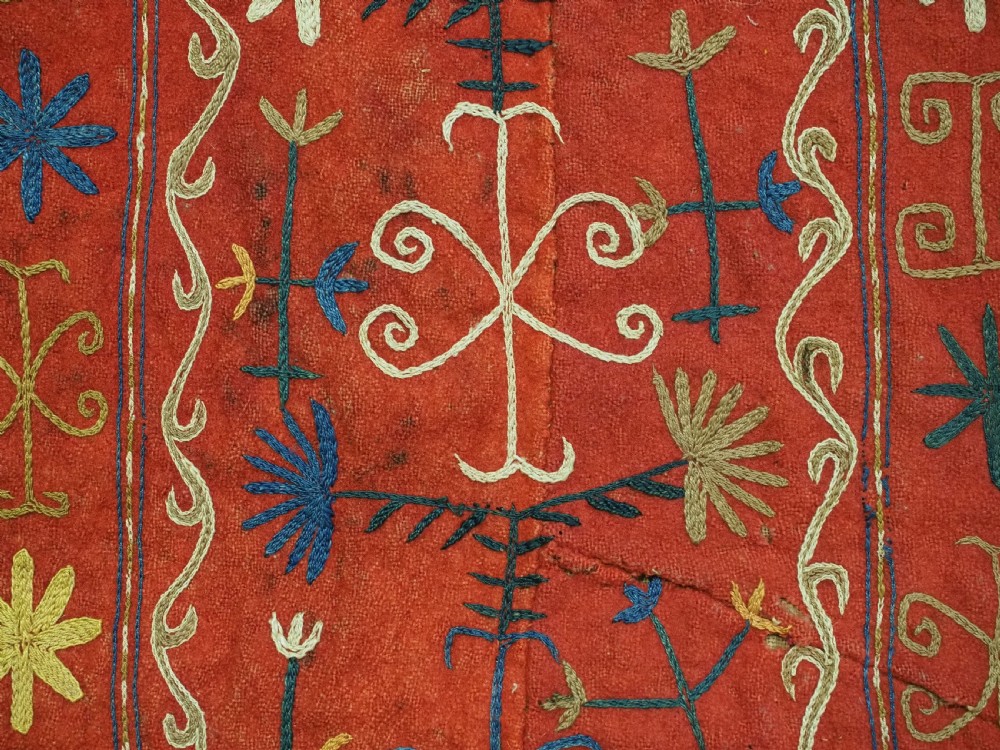 A vibrant red wool embroidered tribal textile bag featuring intricate polychrome scroll motifs in yellow, blue, purple, and green, finished with tassels at the bottom corners. View XII