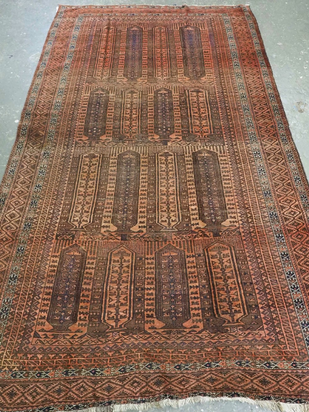 An antique Afghan Baluch hand-knotted wool carpet featuring repeating vertical geometric motifs in terracotta, dark brown, and rust tones.