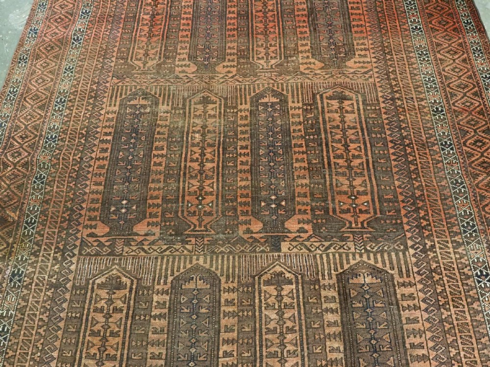 An antique Afghan Baluch hand-knotted wool carpet featuring repeating vertical geometric motifs in terracotta, dark brown, and rust tones. View IV