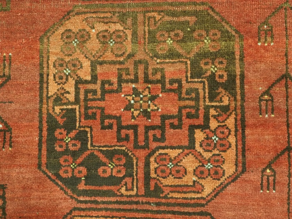 An antique Ersari Turkmen carpet from circa 1890 featuring repeating octagonal guls across a deep terracotta red wool field with geometric borders. View X