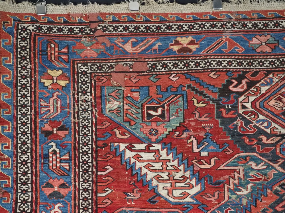 An antique hand-woven Caucasian Soumak flatweave rug featuring a red ground with geometric dragon medallions and a patterned border. View V