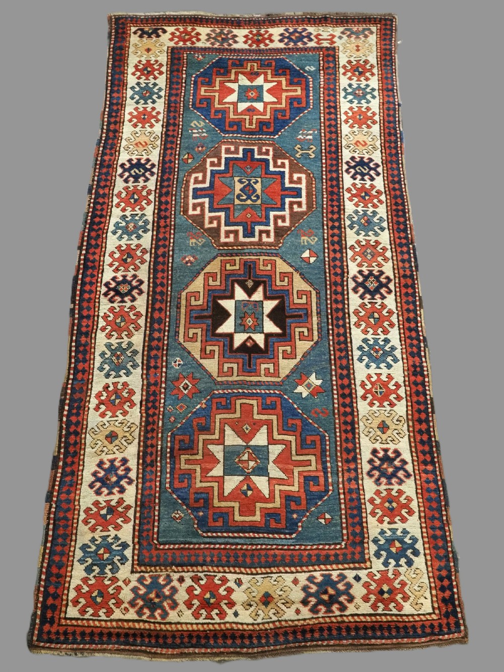 An antique Caucasian Kazak hand-knotted long rug featuring four geometric medallions along a central teal blue field within a decorated ivory border.