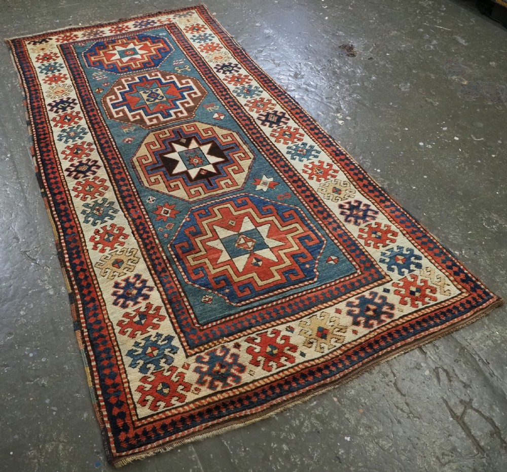 An antique Caucasian Kazak hand-knotted long rug featuring four geometric medallions along a central teal blue field within a decorated ivory border. View II