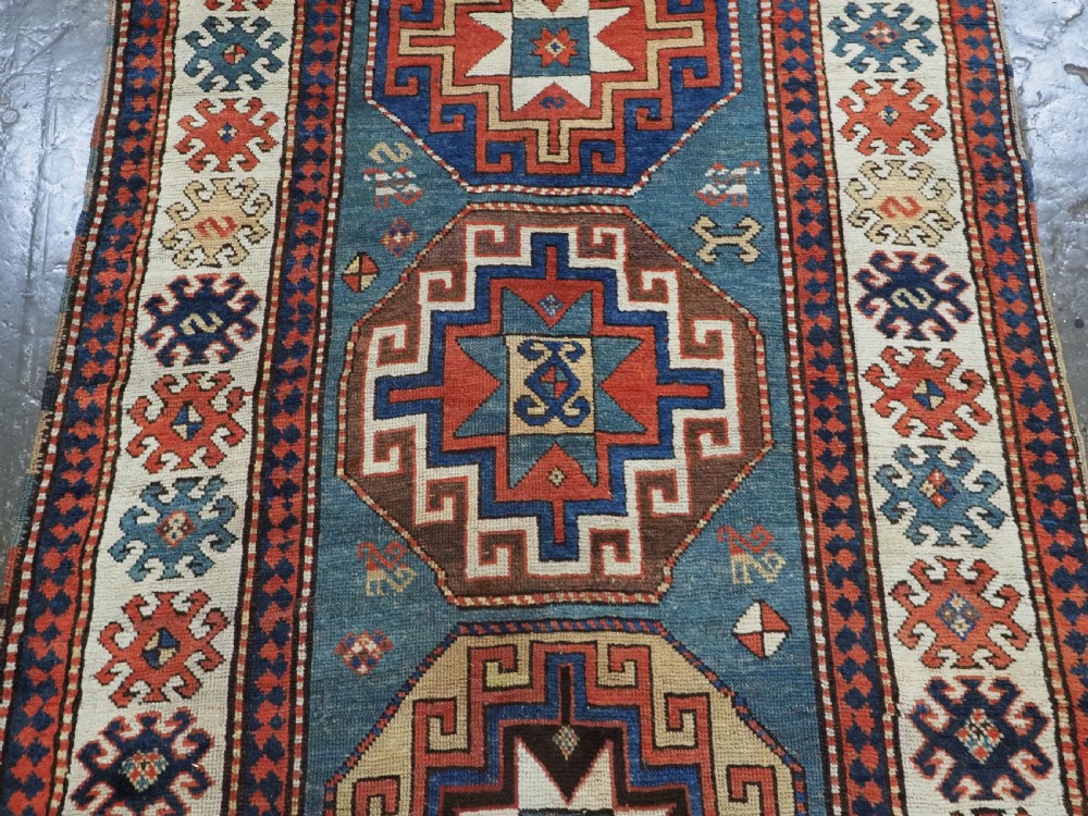 An antique Caucasian Kazak hand-knotted long rug featuring four geometric medallions along a central teal blue field within a decorated ivory border. View IV