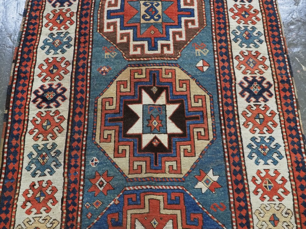 An antique Caucasian Kazak hand-knotted long rug featuring four geometric medallions along a central teal blue field within a decorated ivory border. View V