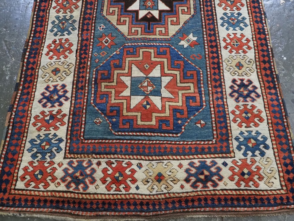 An antique Caucasian Kazak hand-knotted long rug featuring four geometric medallions along a central teal blue field within a decorated ivory border. View VI