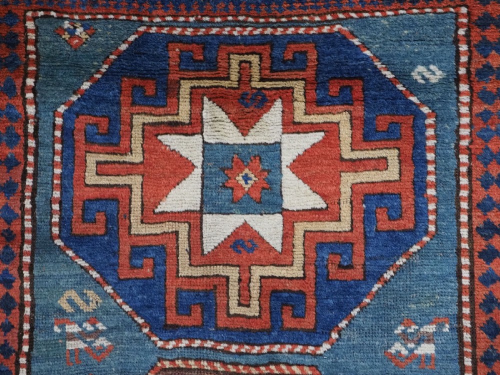 An antique Caucasian Kazak hand-knotted long rug featuring four geometric medallions along a central teal blue field within a decorated ivory border. View IX