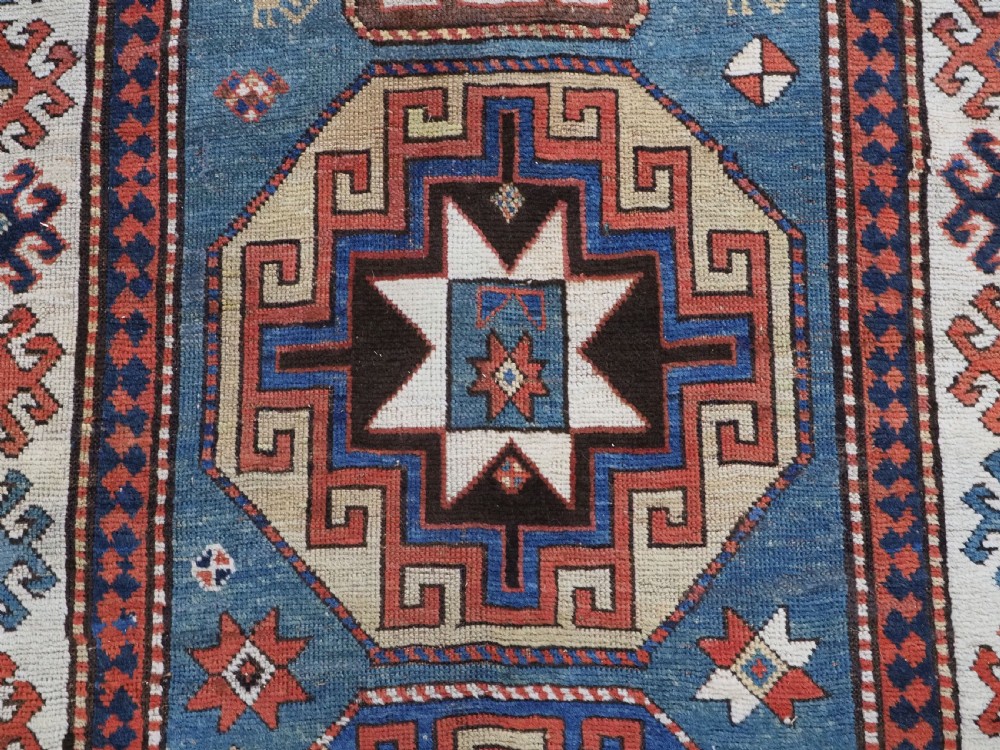 An antique Caucasian Kazak hand-knotted long rug featuring four geometric medallions along a central teal blue field within a decorated ivory border. View XI