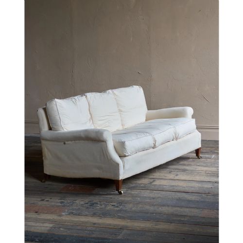 fig 1. A three-seat sofa upholstered in cream calico lining with rolled arms, loose cushions, and short timber legs fitted with brass castors.