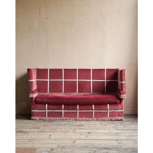 fig 2. A claret red velvet Knole sofa featuring grid pattern braid trim, fringe edging, and adjustable drop-down armrests with metal ratchets.