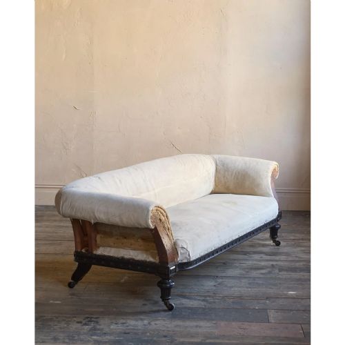 fig 1. An antique Aesthetic Movement Chesterfield sofa featuring off-white upholstery, rolled arms, a dark carved timber frame, and turned legs with castors.