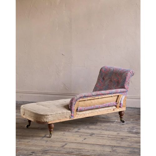 fig 1. An antique Victorian chaise longue by Howard and Sons featuring patterned fabric upholstery, a single armrest, turned legs, and brass castors.