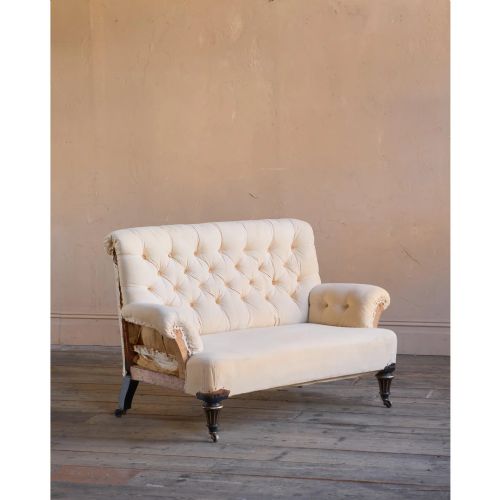 fig 1. A Victorian two-seater sofa featuring deep button-tufted off-white calico upholstery, scroll arms, and turned front legs with brass castors.