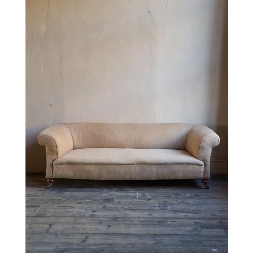 fig 1. A 19th-century Chesterfield sofa upholstered in neutral beige calico fabric featuring rolled arms and turned wooden legs on brass castors.