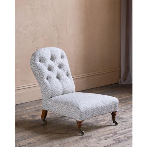fig 1. A low-seated Victorian armless slipper chair upholstered in grey patterned fabric with a button-back design and turned legs on brass castors.