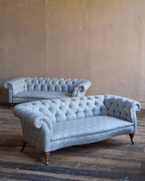 fig 1. A pair of antique serpentine Chesterfield sofas featuring light blue patterned fabric, deep button-tufted backrests, rolled arms, and turned wooden legs on brass castors.