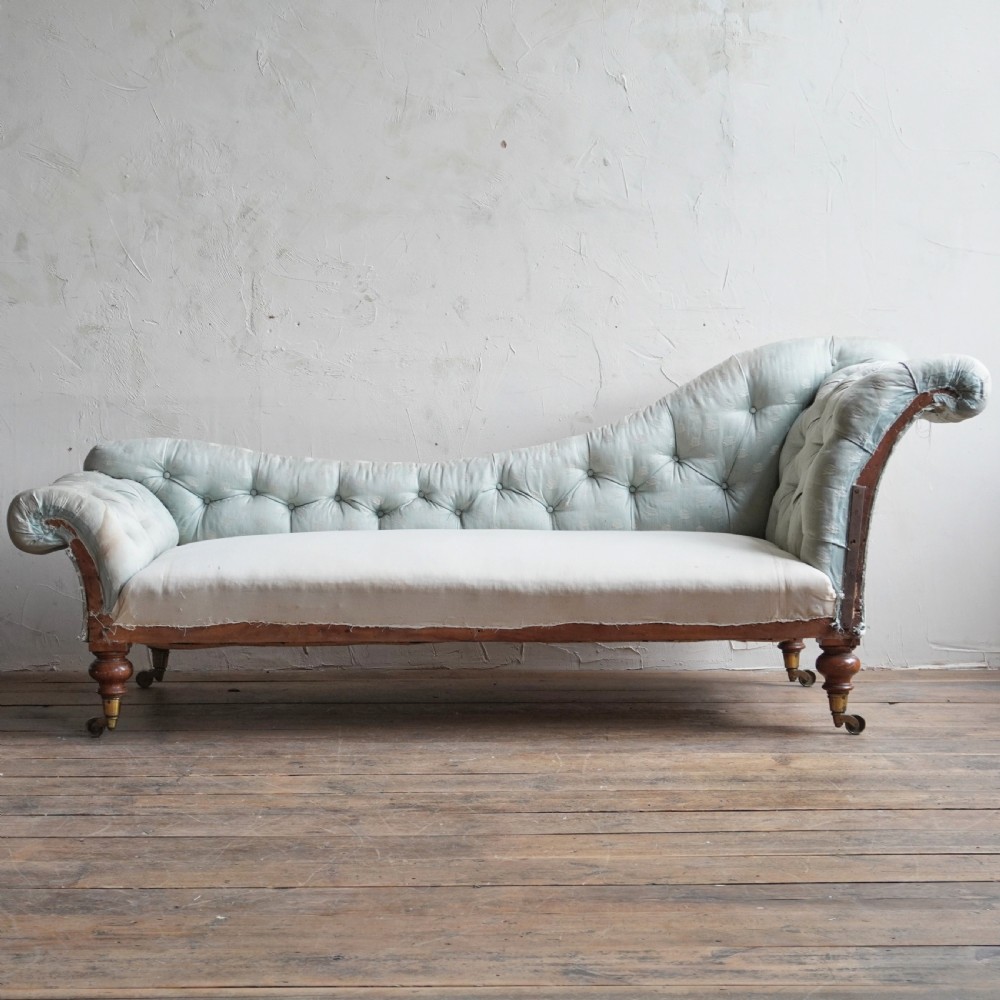 An early Victorian upholstered chaise longue featuring light blue deep-buttoned fabric, a scrolled backrest, and turned wood legs with brass castors. View II