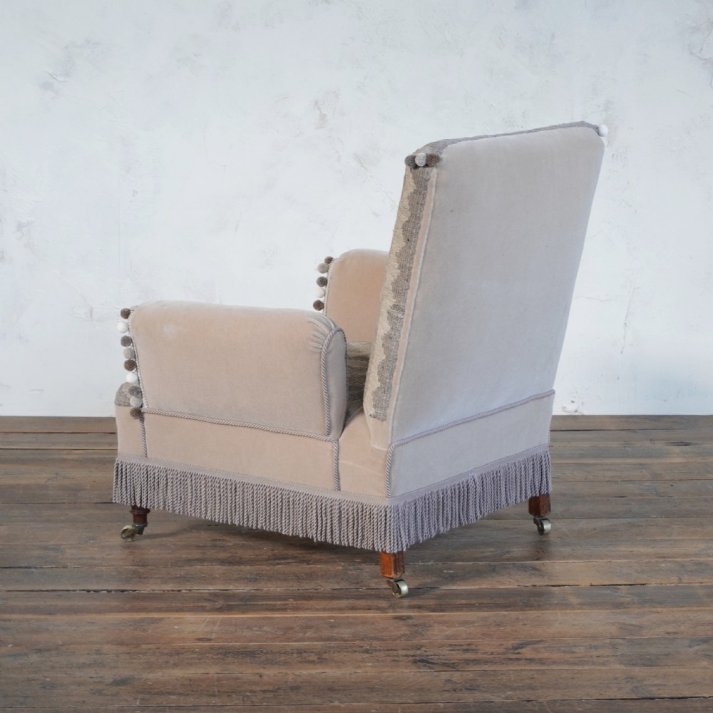 A Victorian style armchair upholstered with grey geometric kilim textile on the backrest and seat, trimmed with beige velvet, pom-poms, fringe, and mounted on turned legs with brass castors. View VII