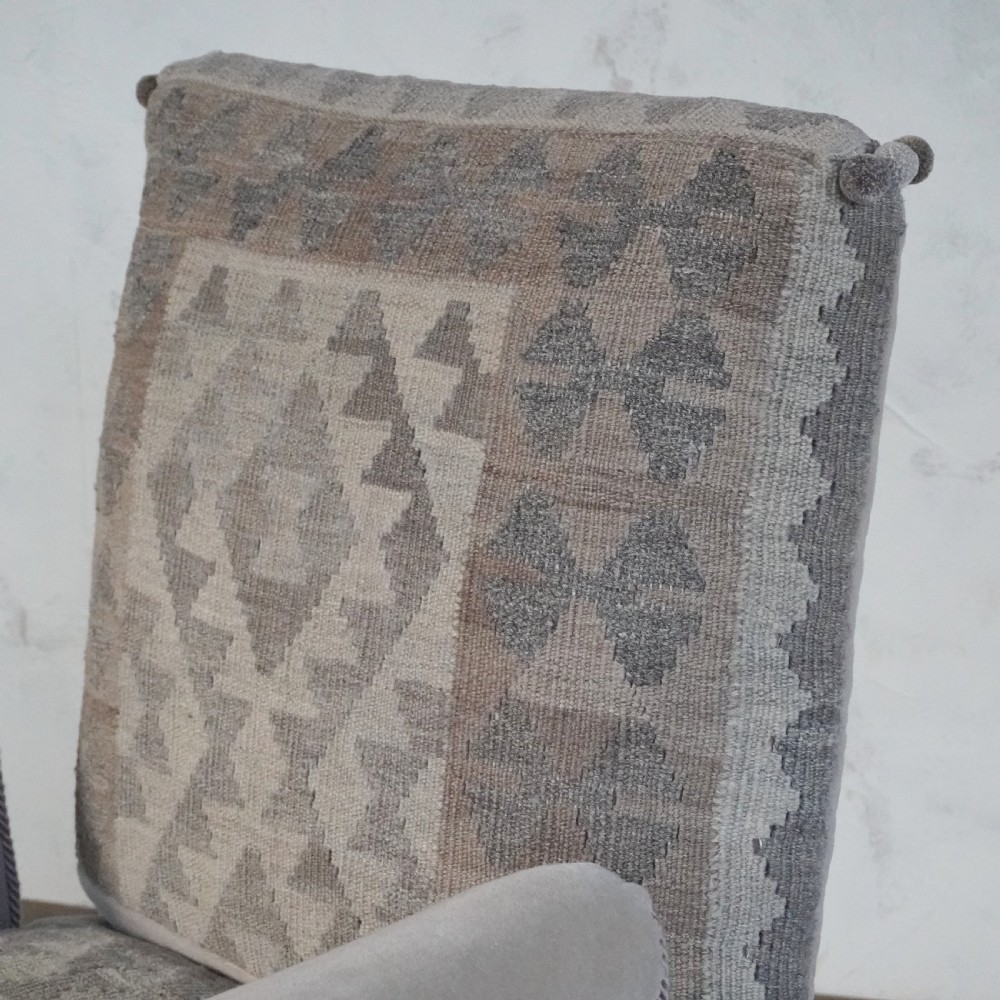 A Victorian style armchair upholstered with grey geometric kilim textile on the backrest and seat, trimmed with beige velvet, pom-poms, fringe, and mounted on turned legs with brass castors. View VIII
