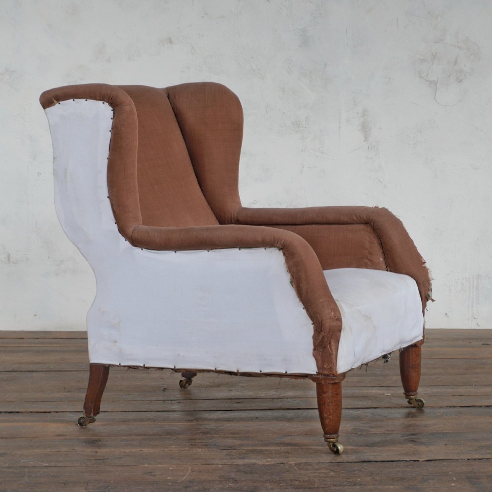A Victorian wingback armchair upholstered in brown fabric and white calico with turned wood legs and brass castors.