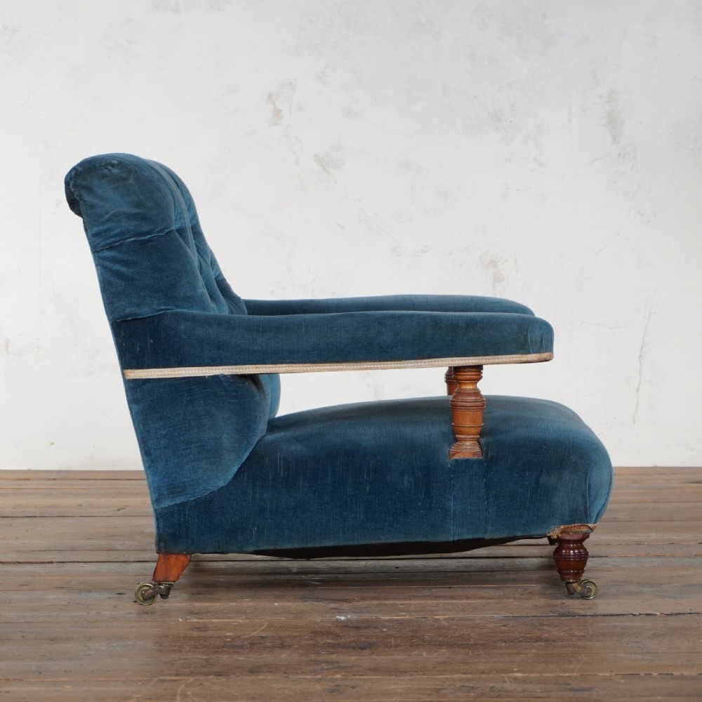 An antique Howard and Sons open armchair upholstered in dark blue velvet, featuring button-tufting on the backrest and turned wooden legs with brass castors. View IX