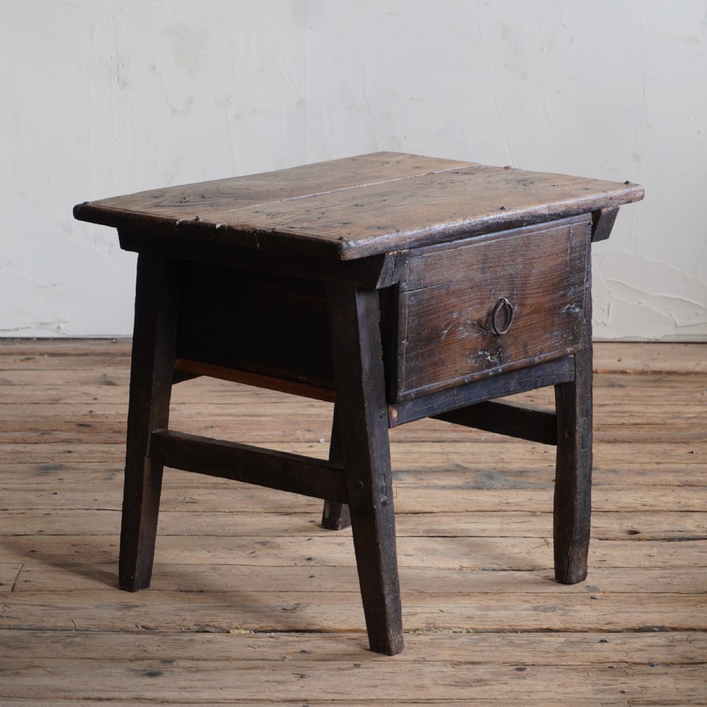 An antique dark walnut Spanish table featuring a single drawer with a ring pull and straight stretcher-supported legs.