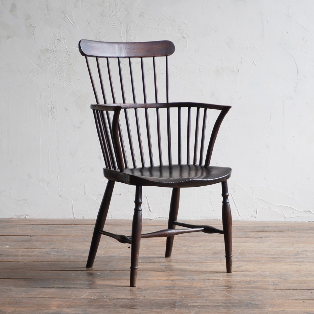 An antique dark wood comb back Windsor armchair with a saddle seat, slender vertical spindles, and turned legs joined by stretchers.