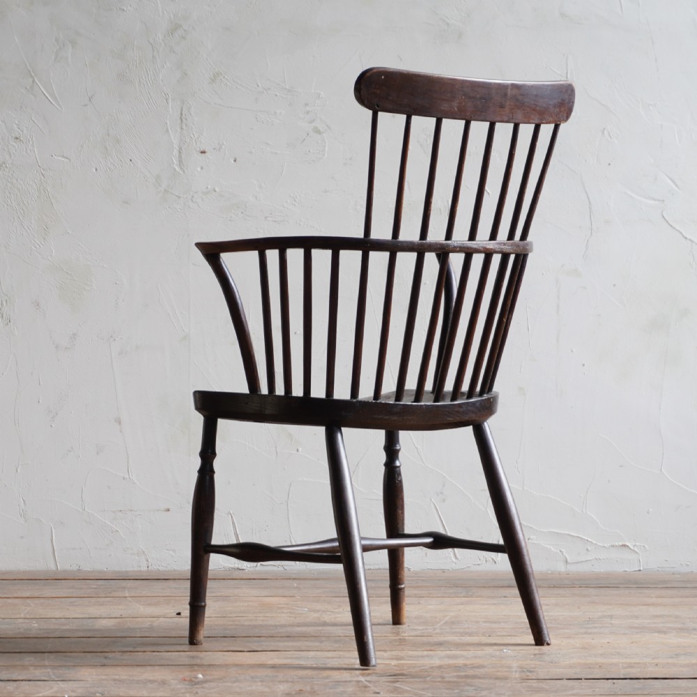 An antique dark wood comb back Windsor armchair with a saddle seat, slender vertical spindles, and turned legs joined by stretchers. View II