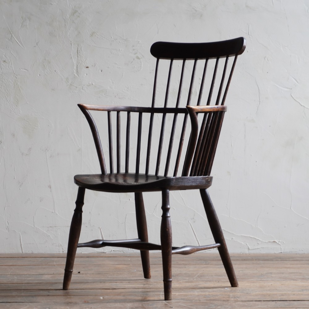 An antique dark wood comb back Windsor armchair with a saddle seat, slender vertical spindles, and turned legs joined by stretchers. View III