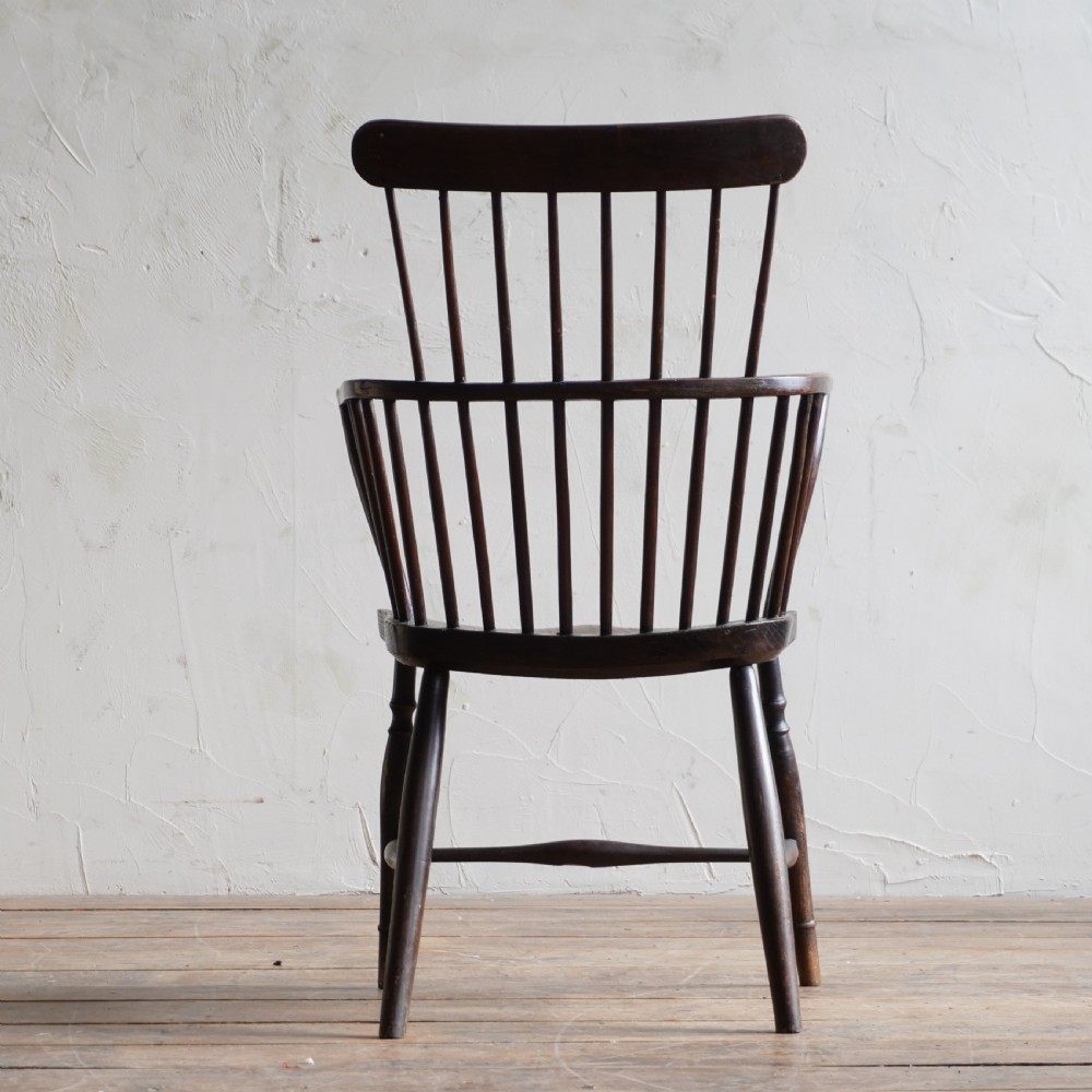 An antique dark wood comb back Windsor armchair with a saddle seat, slender vertical spindles, and turned legs joined by stretchers. View IV