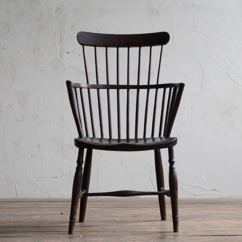 An antique dark wood comb back Windsor armchair with a saddle seat, slender vertical spindles, and turned legs joined by stretchers. View V