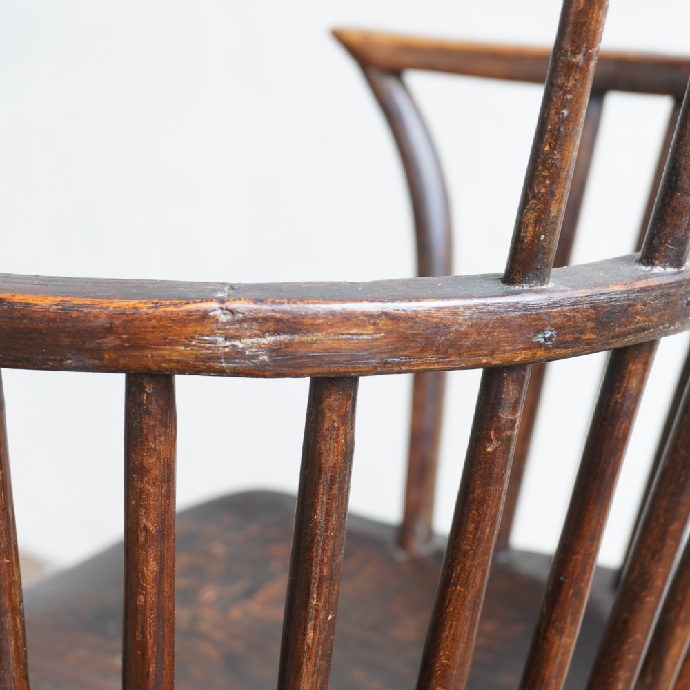An antique dark wood comb back Windsor armchair with a saddle seat, slender vertical spindles, and turned legs joined by stretchers. View VIII