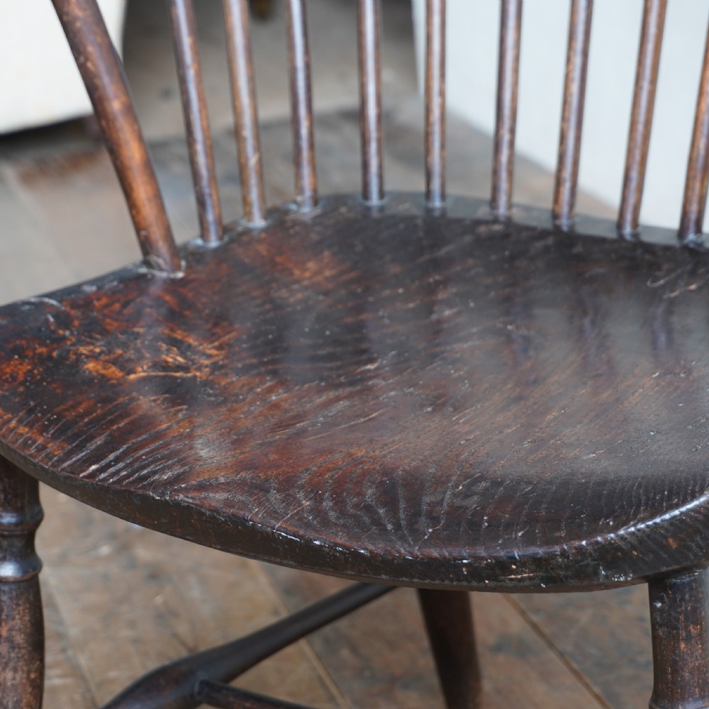 An antique dark wood comb back Windsor armchair with a saddle seat, slender vertical spindles, and turned legs joined by stretchers. View X