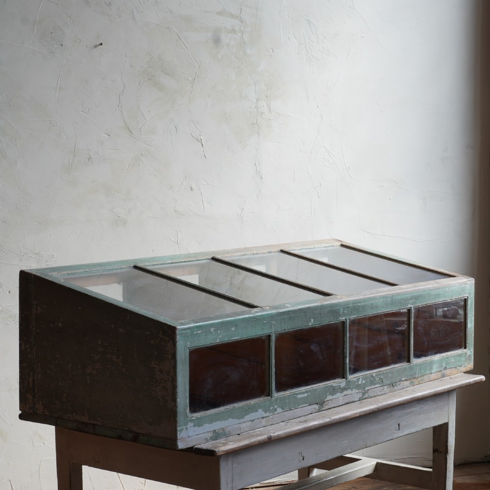 An antique sloped countertop display cabinet featuring four glazed compartments and a distressed green painted timber frame. View III