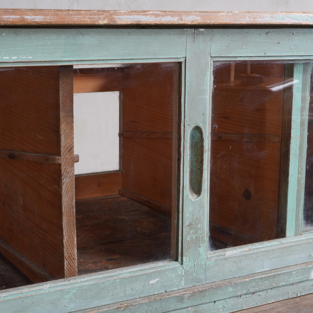 An antique sloped countertop display cabinet featuring four glazed compartments and a distressed green painted timber frame. View IV