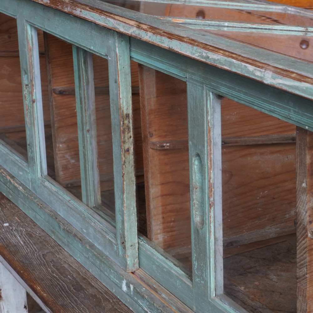 An antique sloped countertop display cabinet featuring four glazed compartments and a distressed green painted timber frame. View V