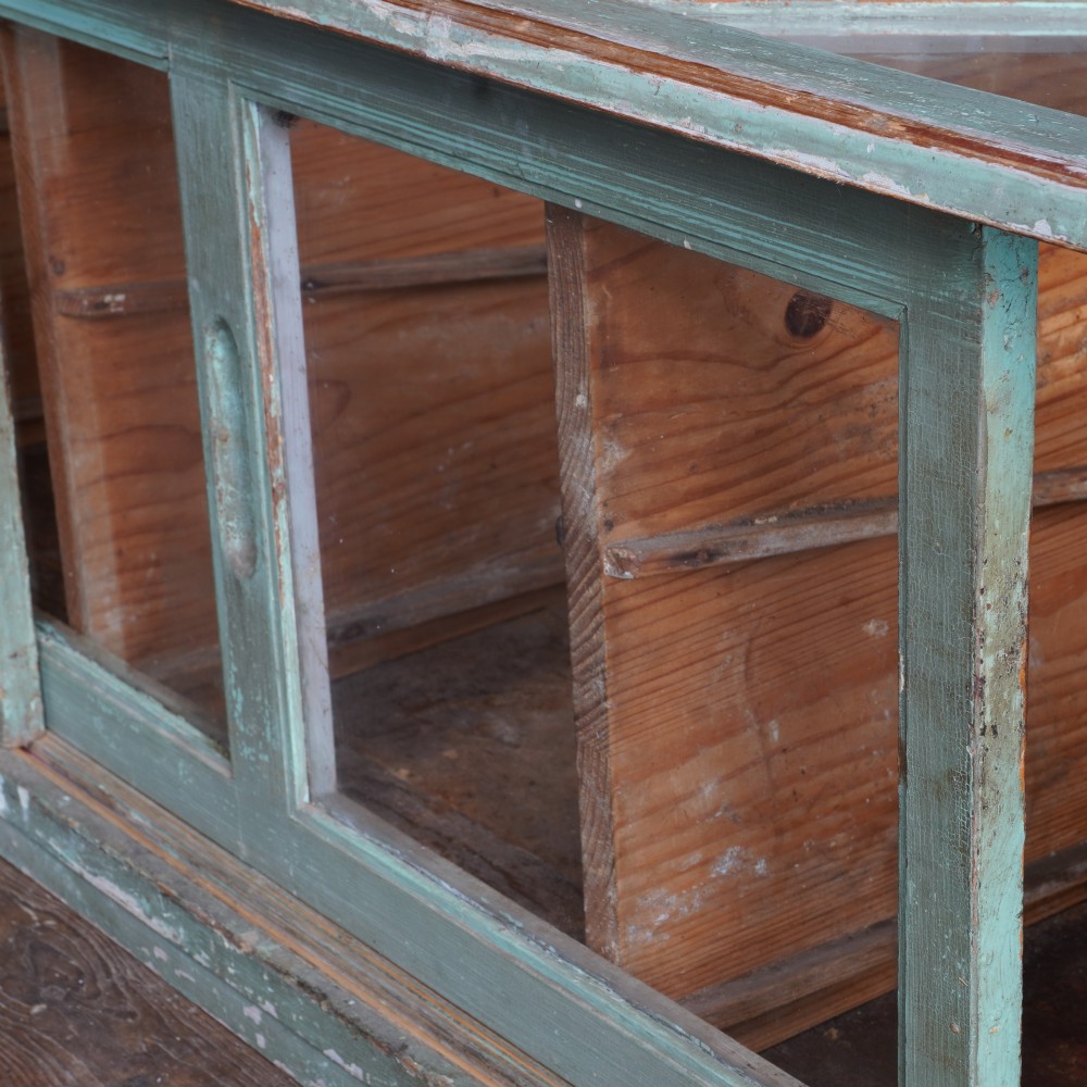 An antique sloped countertop display cabinet featuring four glazed compartments and a distressed green painted timber frame. View II