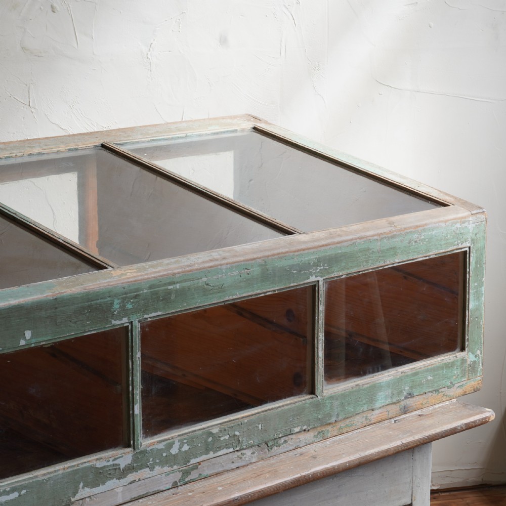 An antique sloped countertop display cabinet featuring four glazed compartments and a distressed green painted timber frame. View VI