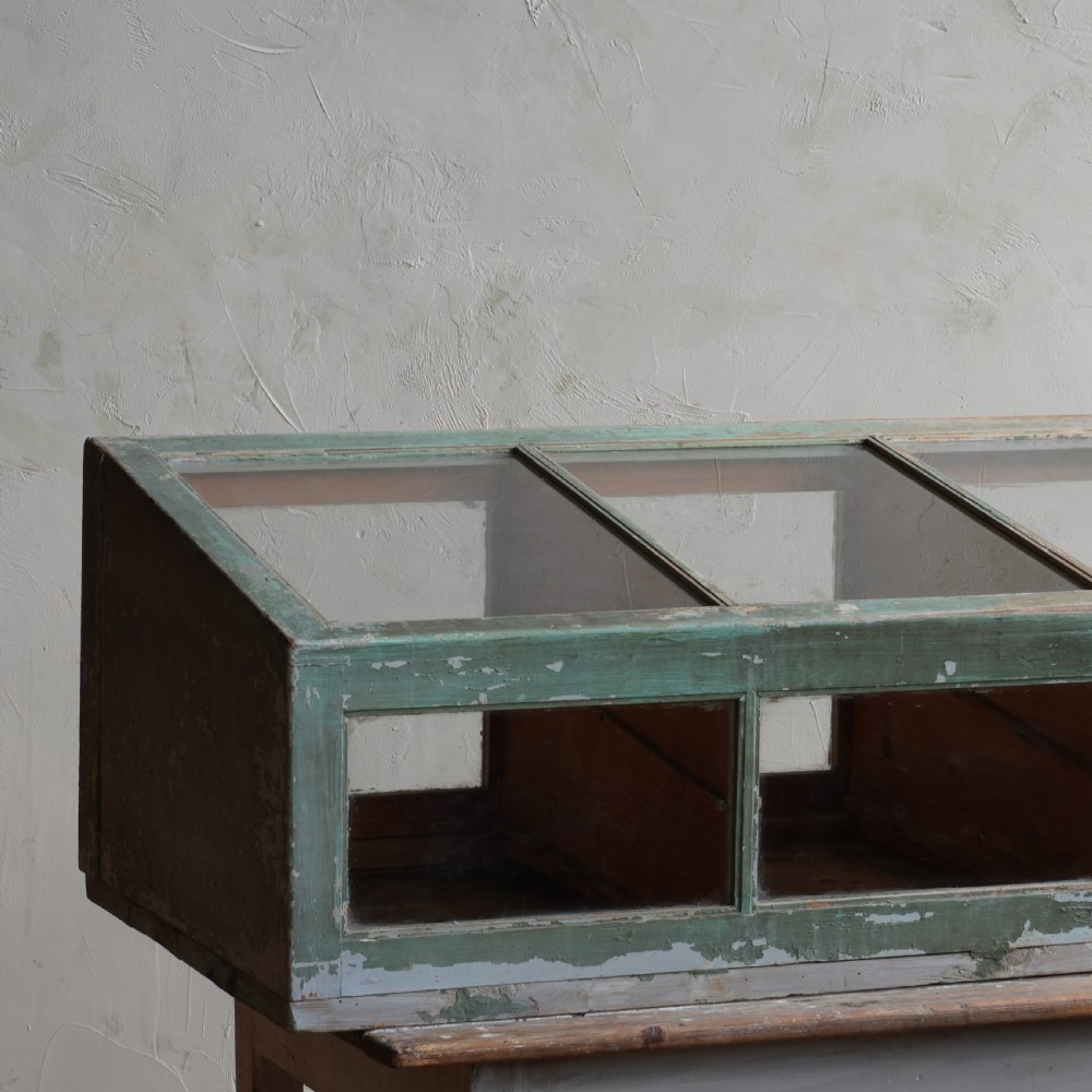 An antique sloped countertop display cabinet featuring four glazed compartments and a distressed green painted timber frame. View VII