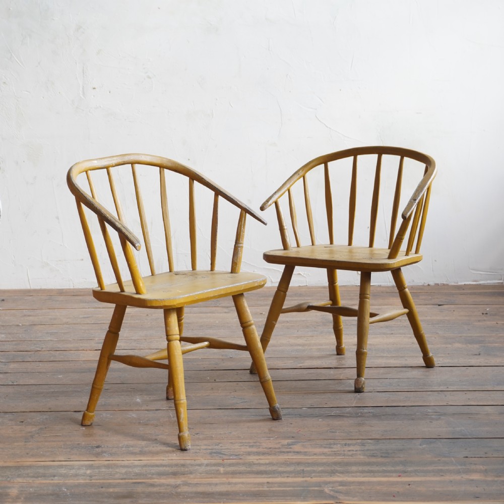 A pair of low-back wooden Windsor armchairs painted in a worn mustard yellow finish, featuring stick backs and turned legs.