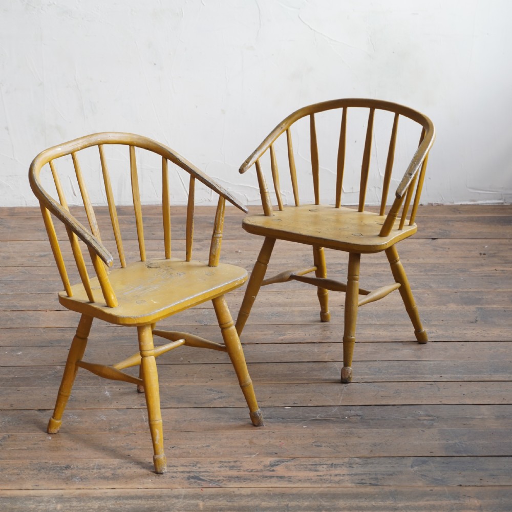 A pair of low-back wooden Windsor armchairs painted in a worn mustard yellow finish, featuring stick backs and turned legs. View II