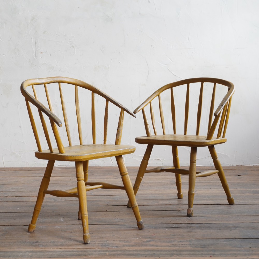 A pair of low-back wooden Windsor armchairs painted in a worn mustard yellow finish, featuring stick backs and turned legs. View III