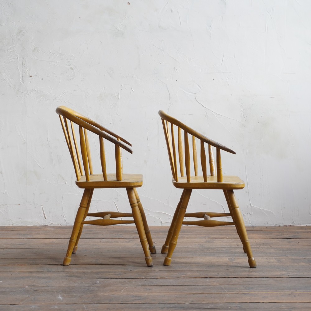 A pair of low-back wooden Windsor armchairs painted in a worn mustard yellow finish, featuring stick backs and turned legs. View V