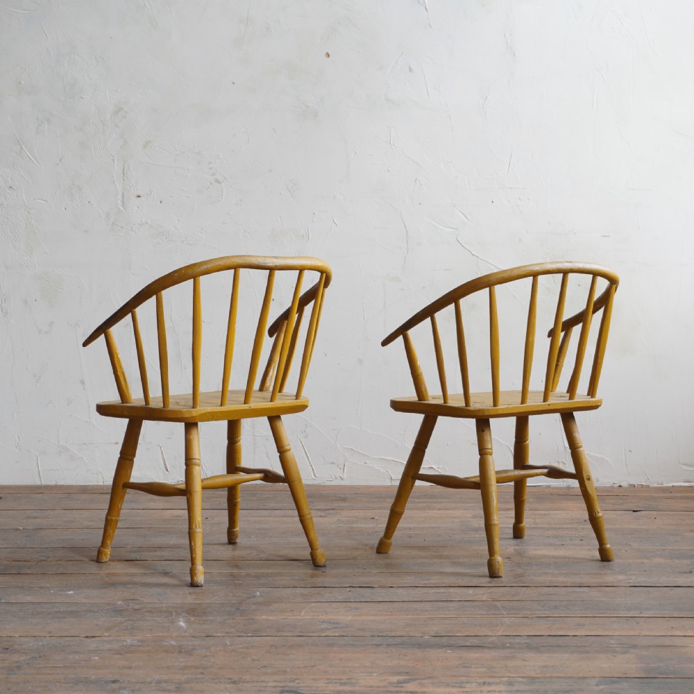 A pair of low-back wooden Windsor armchairs painted in a worn mustard yellow finish, featuring stick backs and turned legs. View VI