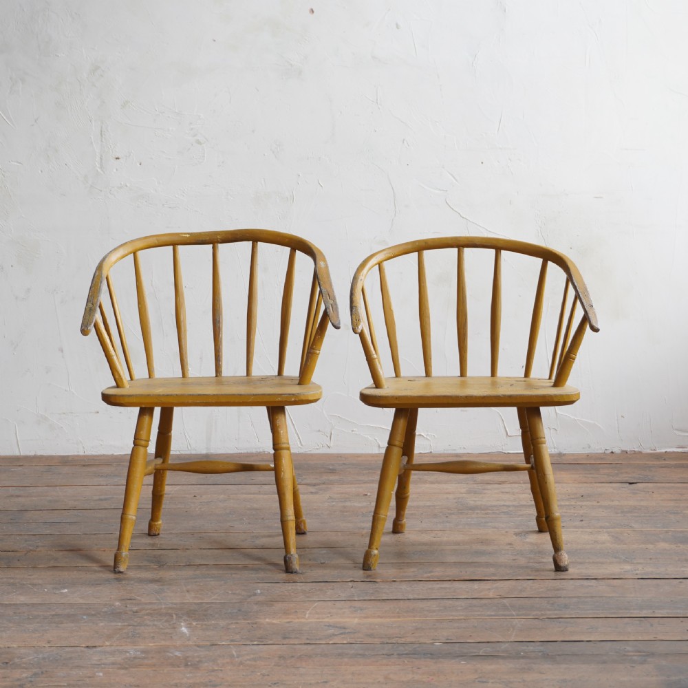 A pair of low-back wooden Windsor armchairs painted in a worn mustard yellow finish, featuring stick backs and turned legs. View VII