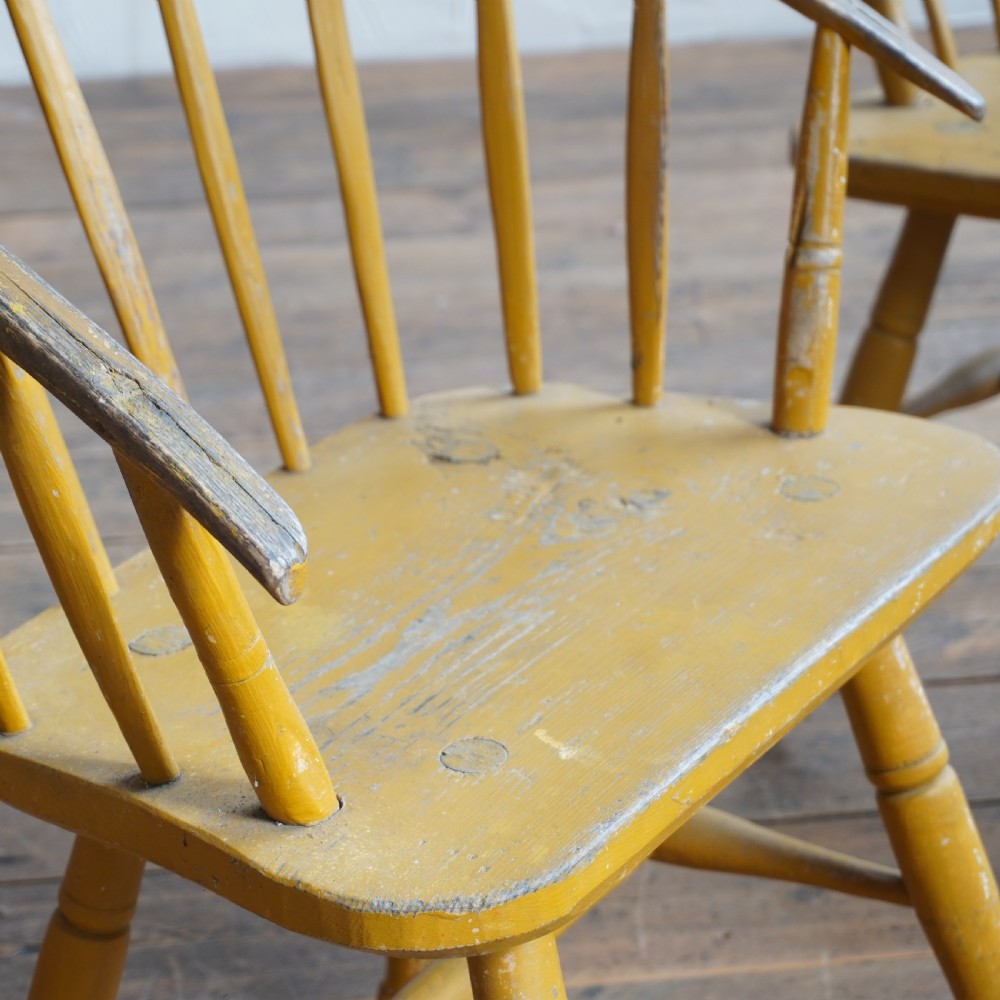 A pair of low-back wooden Windsor armchairs painted in a worn mustard yellow finish, featuring stick backs and turned legs. View X