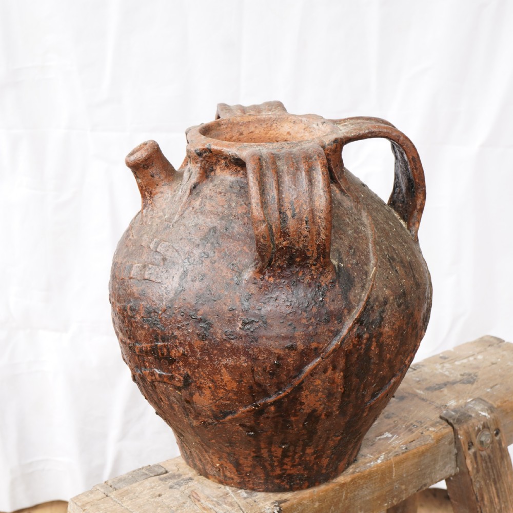 A rustic brown terracotta oil jug featuring a small spout, sturdy side handles, and incised horizontal banding on its bulbous body. View II