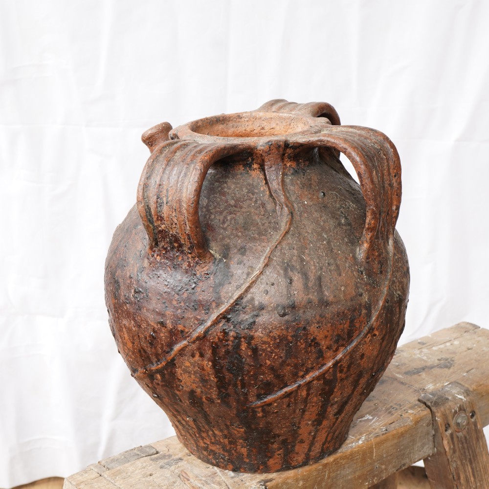 A rustic brown terracotta oil jug featuring a small spout, sturdy side handles, and incised horizontal banding on its bulbous body. View III
