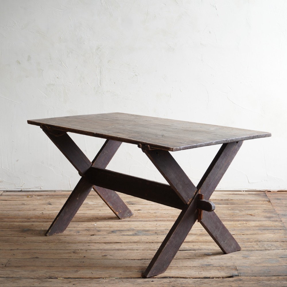 A rustic dark timber tavern table featuring an X-frame trestle base connected by a central horizontal stretcher.