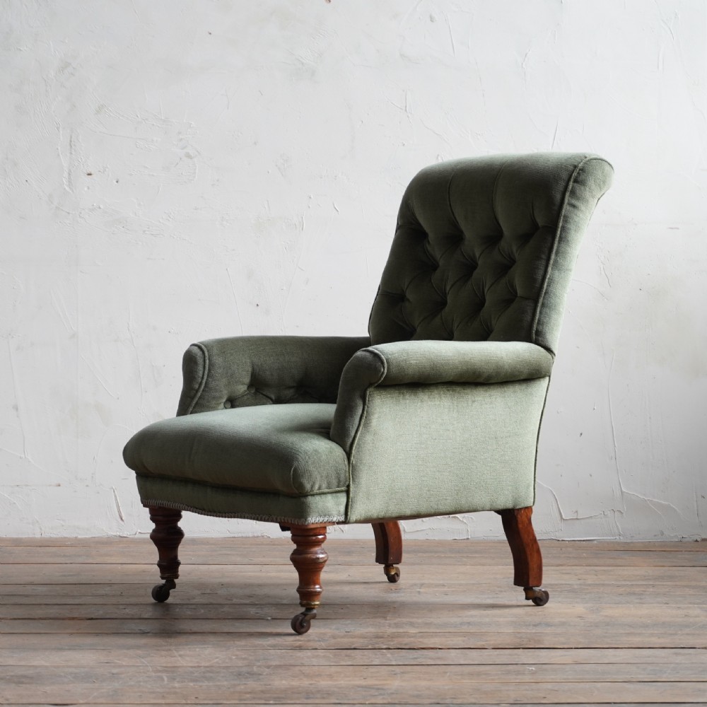 An antique green velvet armchair with button tufting, turned wooden legs, and brass castors.